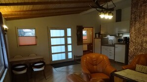 Una sala de estar con sofá, una mesa de comedor con sillas, una zona de cocina con armarios y electrodomésticos, y una puerta que da a otra habitación.