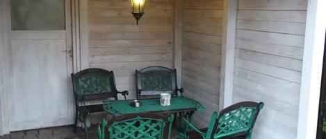 A covered outdoor seating area with a table and four chairs, a hanging lantern, and a wall-mounted drying rack.