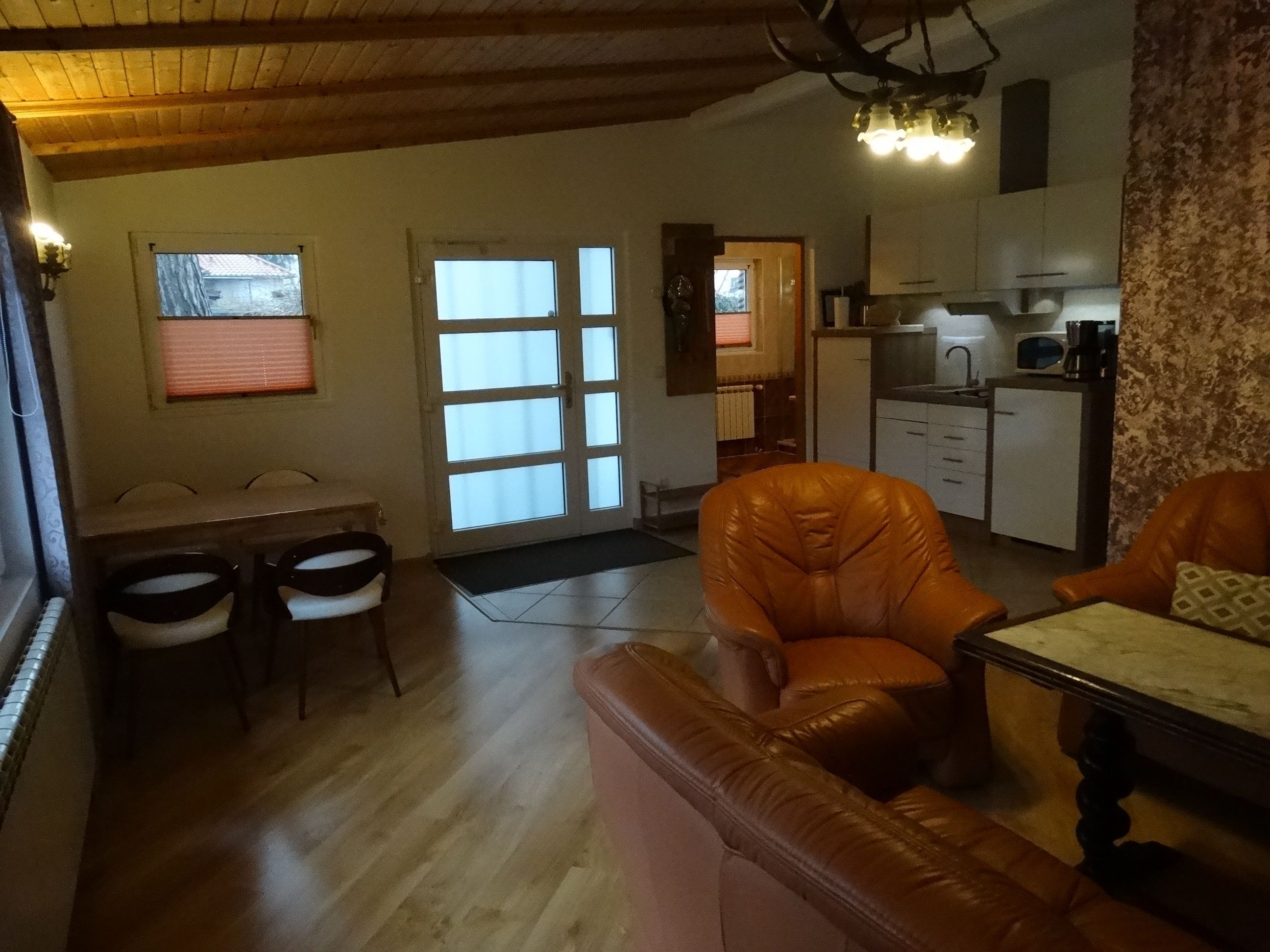 A living room with a sofa, a dining table with chairs, a kitchen area with cabinets and appliances, and a door leading to another room.