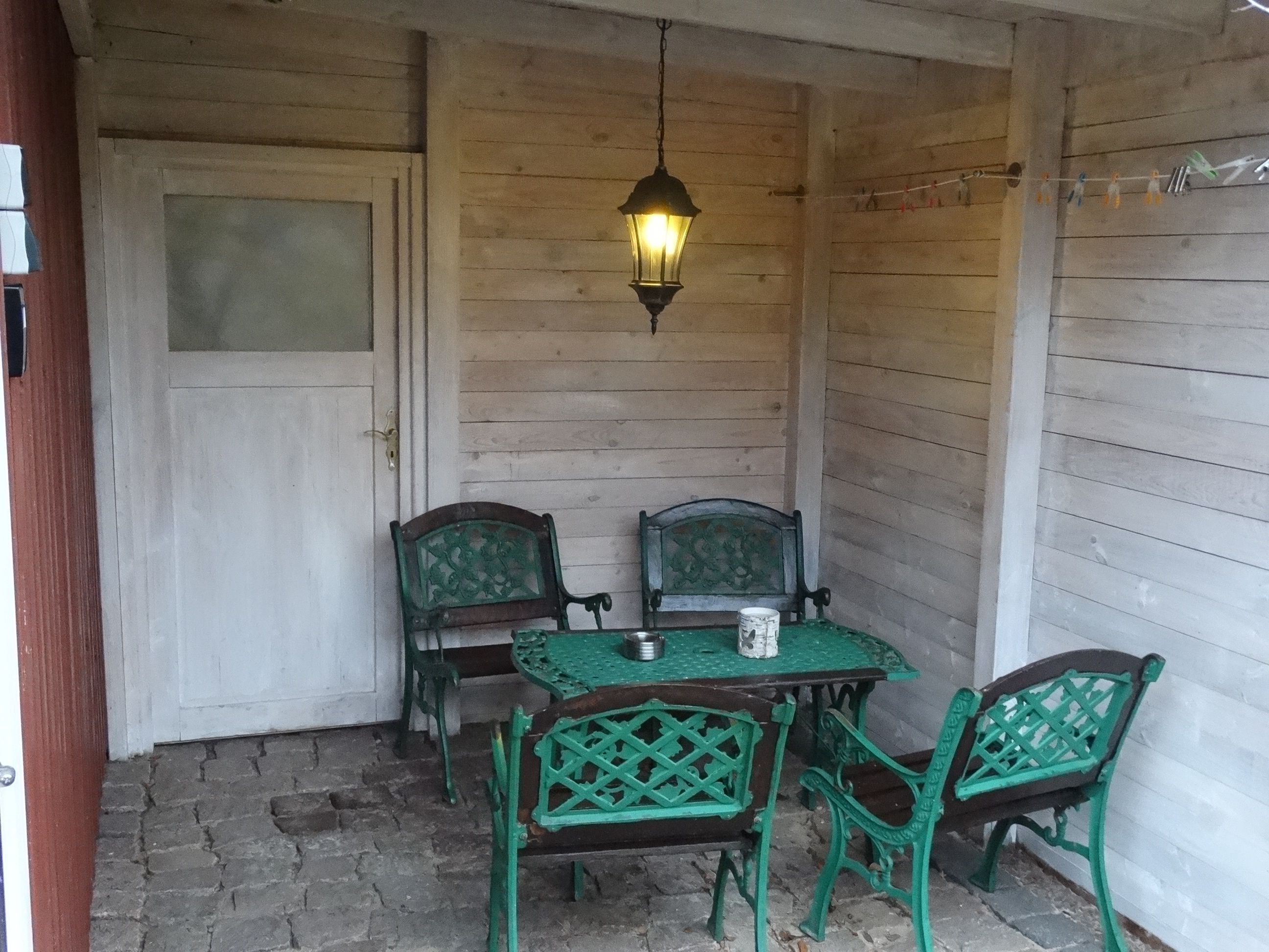 Un portico in legno con tavolo e sedie, un lampione appeso e una porta.