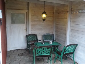 A wooden porch with a table and chairs, a hanging lantern, and a door.