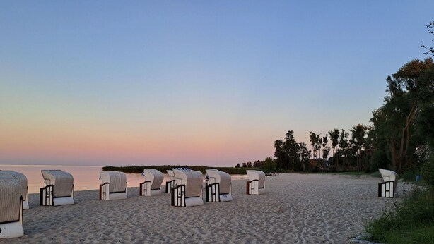 Una playa con filas de sillas blancas para tomar el sol y un muro de piedra.