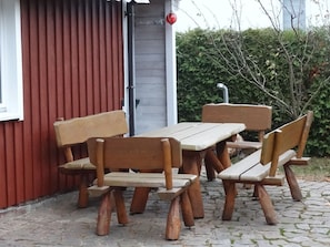 A wooden outdoor seating area with benches and a table, adjacent to a red building with a white window and a door. - Schwedenhaus - FH Schwedenhaus (Mönkebude)