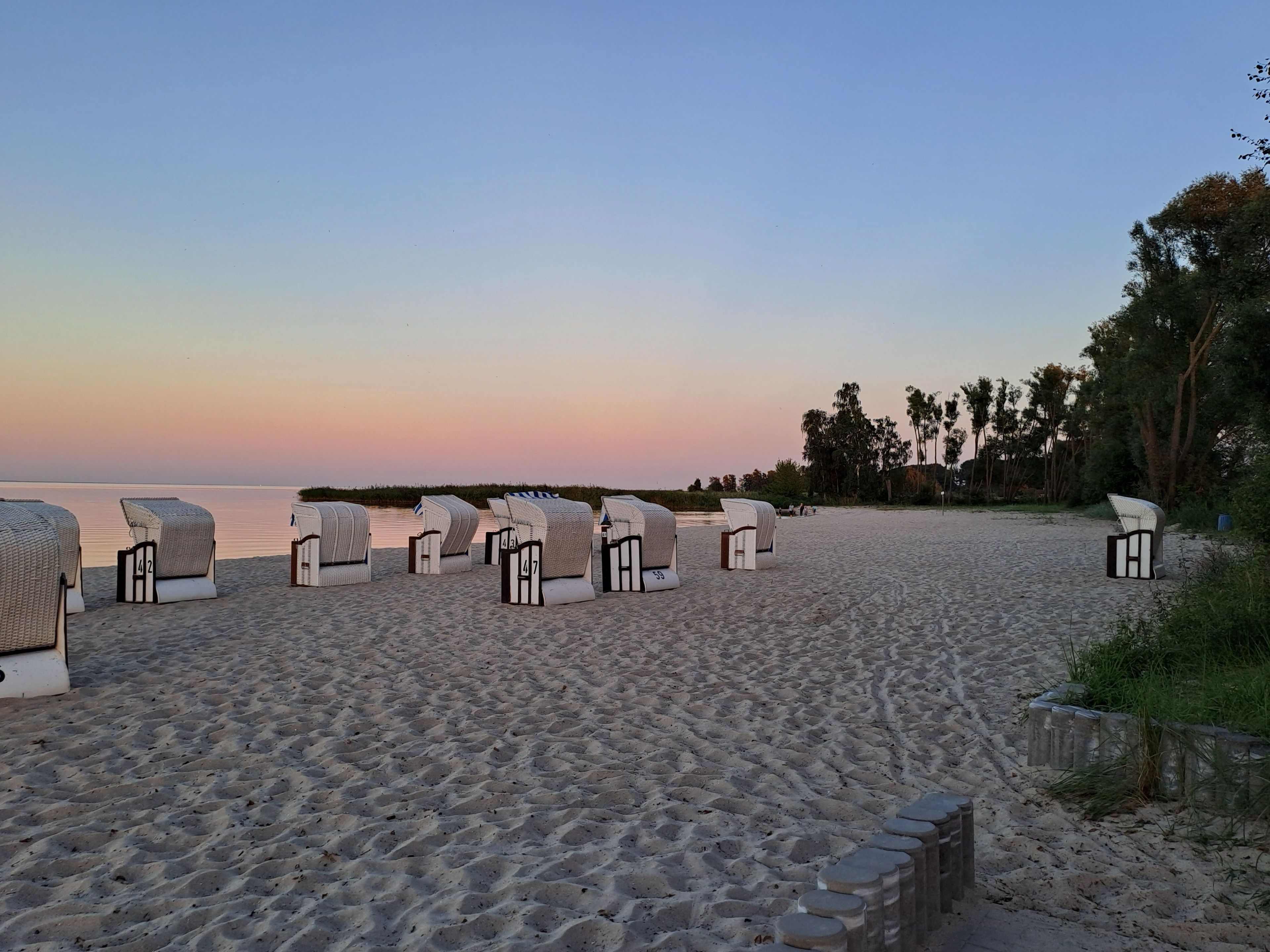 A beach with rows of white lounge chairs and a stone wall.