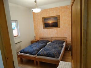 A bedroom with a wooden bed, a nightstand, a wall-mounted painting, and a window with blinds. - Schwedenhaus - FH Schwedenhaus (Mönkebude)