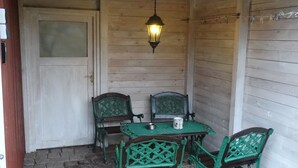 Un porche de madera con una mesa, sillas, un farol colgante y una puerta.