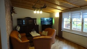 Una sala de estar con piso de madera, una araña, un televisor y dos sillones de cuero.