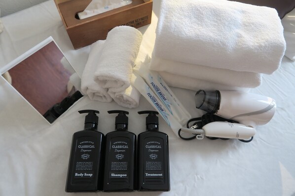 Une salle de bain bien rangée, avec une serviette blanche, un sèche-cheveux et trois flacons de produits de toilette de la gamme « Style vintage classique ».