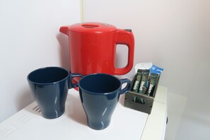 Une machine à café rouge, deux tasses bleues et une boîte de capsules de café Blendr sur un plan de travail blanc.