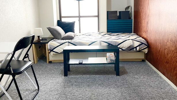 Un dormitorio con cama, escritorio, silla y ventana con cortina azul.