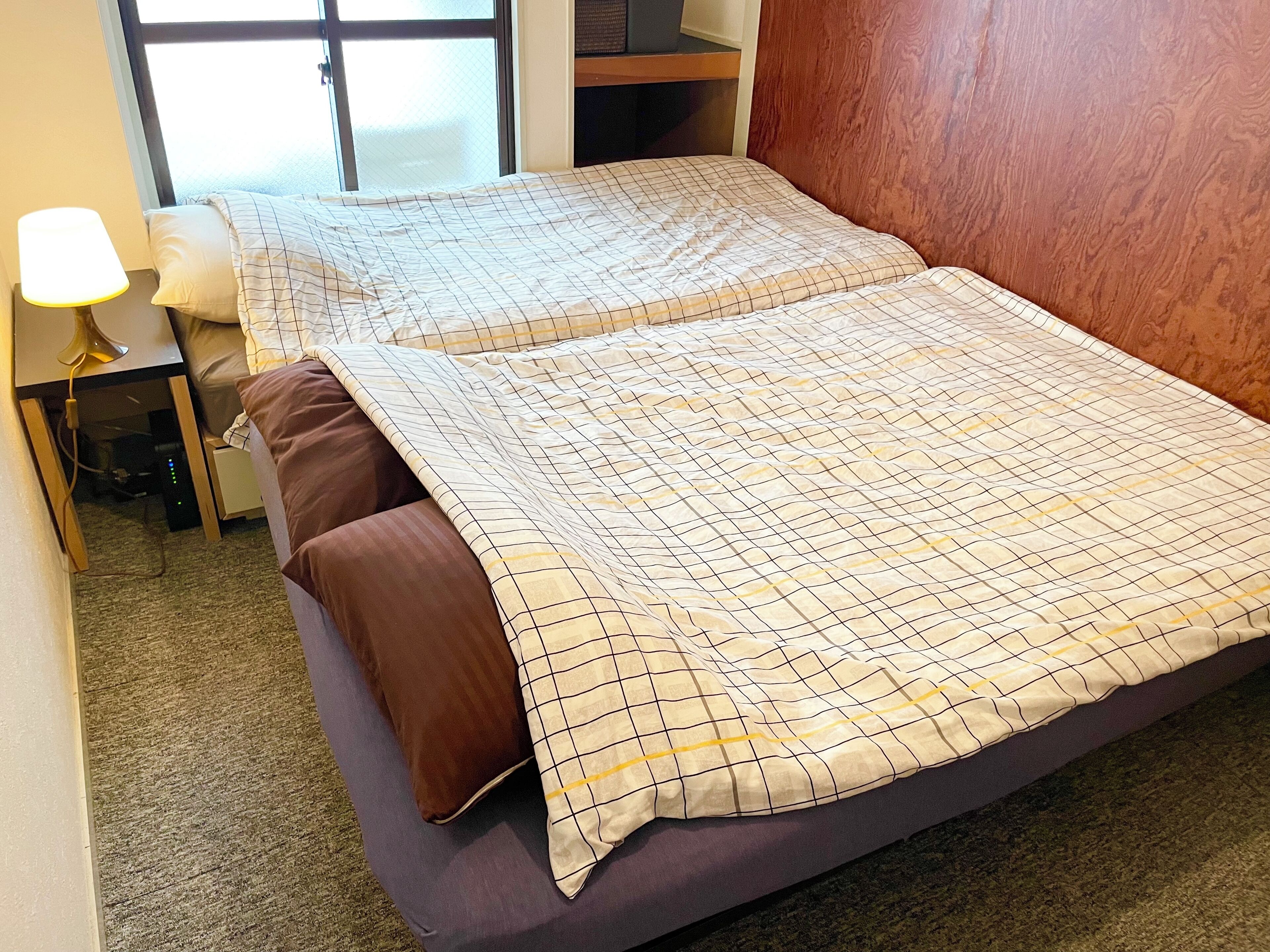 A bed with a checkered bedspread, a brown pillow, and a lamp on a nightstand.