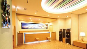 A hotel reception area with a modern design, featuring a reception desk, two chairs, a large wall-mounted TV, and a circular ceiling light fixture. - Ab Hotel Kamagori (Gamagori)