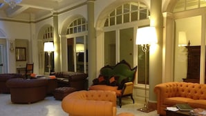 Un vestíbulo amplio con una zona de estar grande, con sofás naranjas y un sillón verde. Dos lámparas de pie proporcionan iluminación.