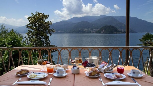 Una mesa preparada con alimentos para el desayuno y una vista panorámica de un lago y montañas.