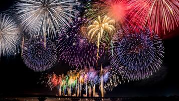 A nighttime view of fireworks over a body of water with reflections on the water's surface.