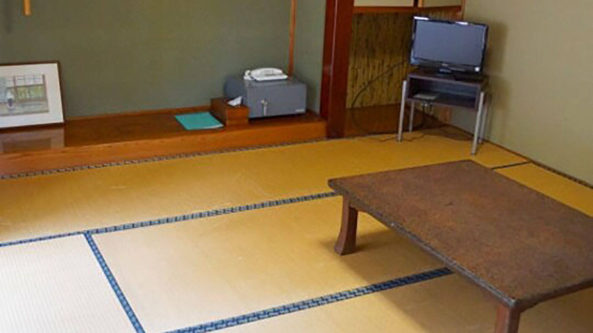 A tatami mat room with a low table, a television on a stand, and a small cabinet.