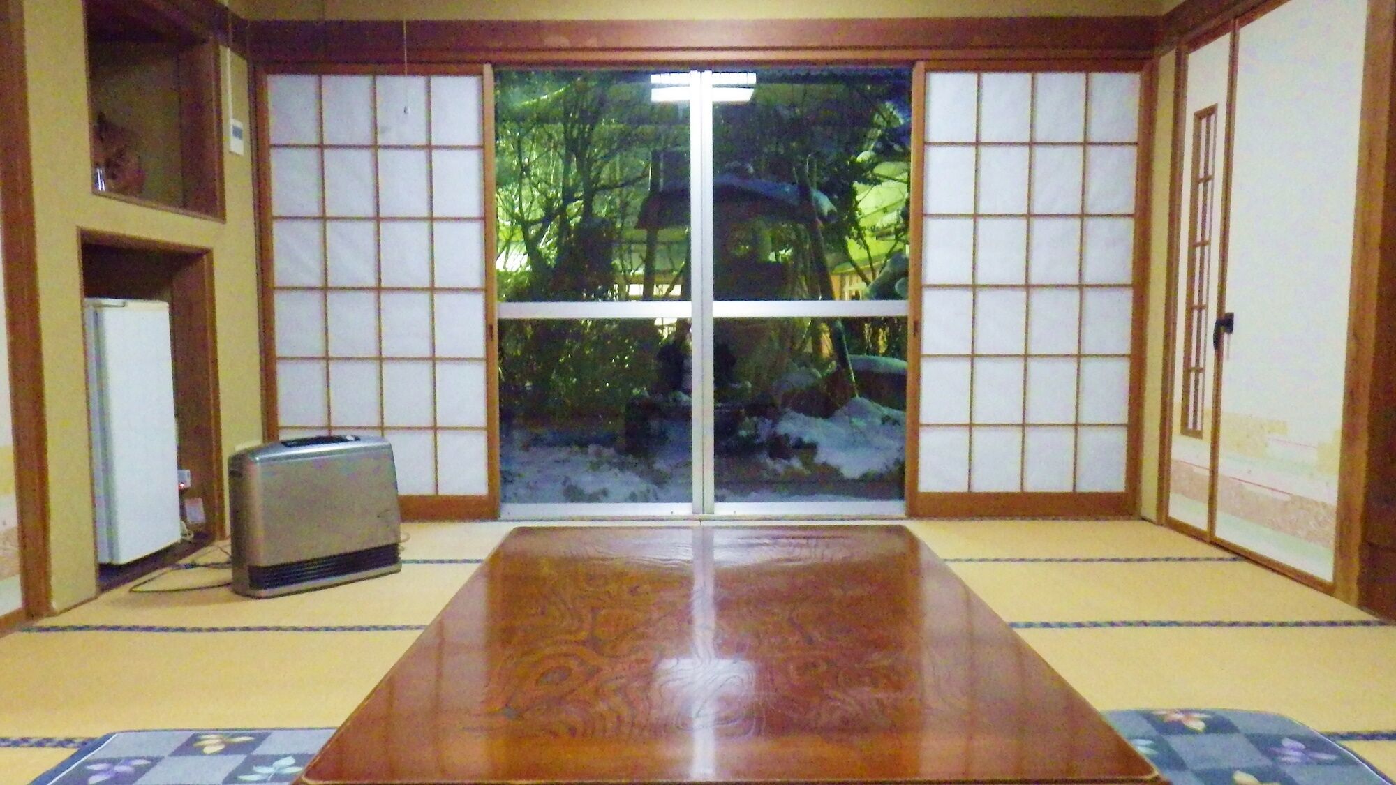 A traditional Japanese room with tatami flooring, sliding doors, a refrigerator, and a toaster.