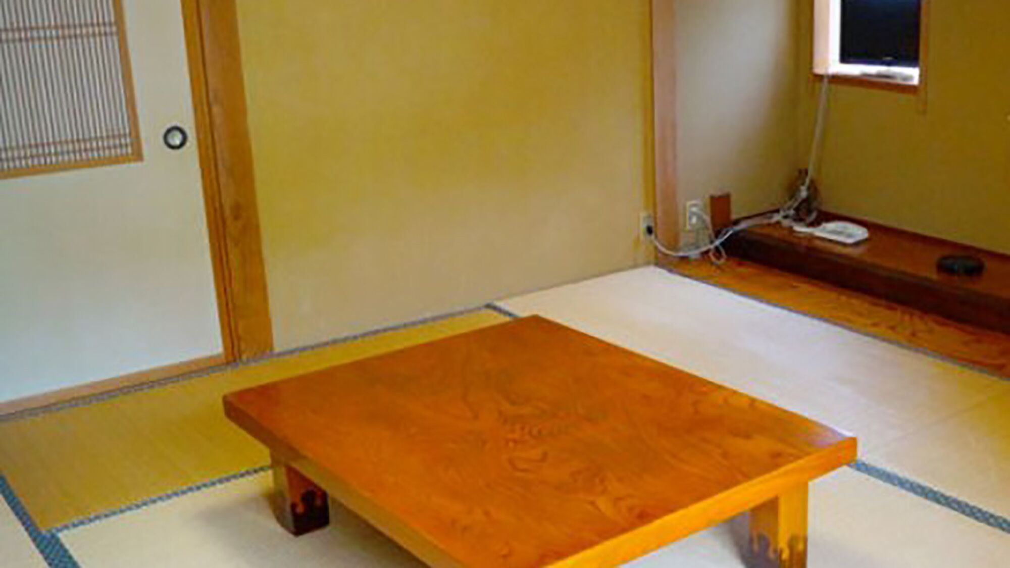 A tatami mat room with a wooden table, a wall-mounted TV, and a power outlet.