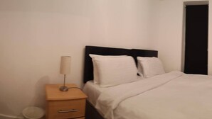 Un dormitorio con cama, mesita de noche con lámpara y una cómoda pequeña.