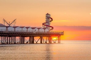 A pier with a series of white buildings, a tall structure with a spiral staircase, and a sunset in the background.