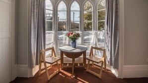 A bay window with three arched windows, a wooden table with two chairs, and a vase with flowers. - Elegant Georgian 1 Bed Apartment in Herne Bay (Herne Bay)