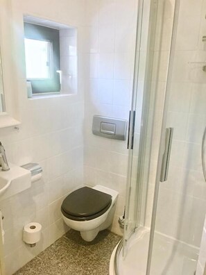 Uma casa de banho pequena e moderna, com sanita, lavatório e chuveiro.