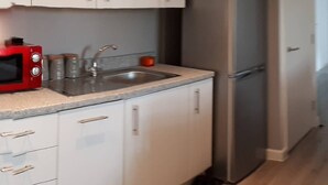 A kitchen with white cabinets, a stainless steel sink, a red microwave, and a silver refrigerator. - Riverside 5 (Maidstone)