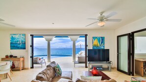 A spacious living room with a large sofa, a television, and a view of the ocean through an open door. - Dream Villa Shore Point 552 (Lowlands)