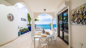 A covered patio with a table set for dining, a view of the ocean, and a painting on the wall. - Dream Villa Shore Point 552 (Lowlands)