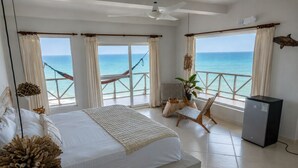 Un dormitorio con cama, una silla, una mesita, refrigerador y vista al océano.