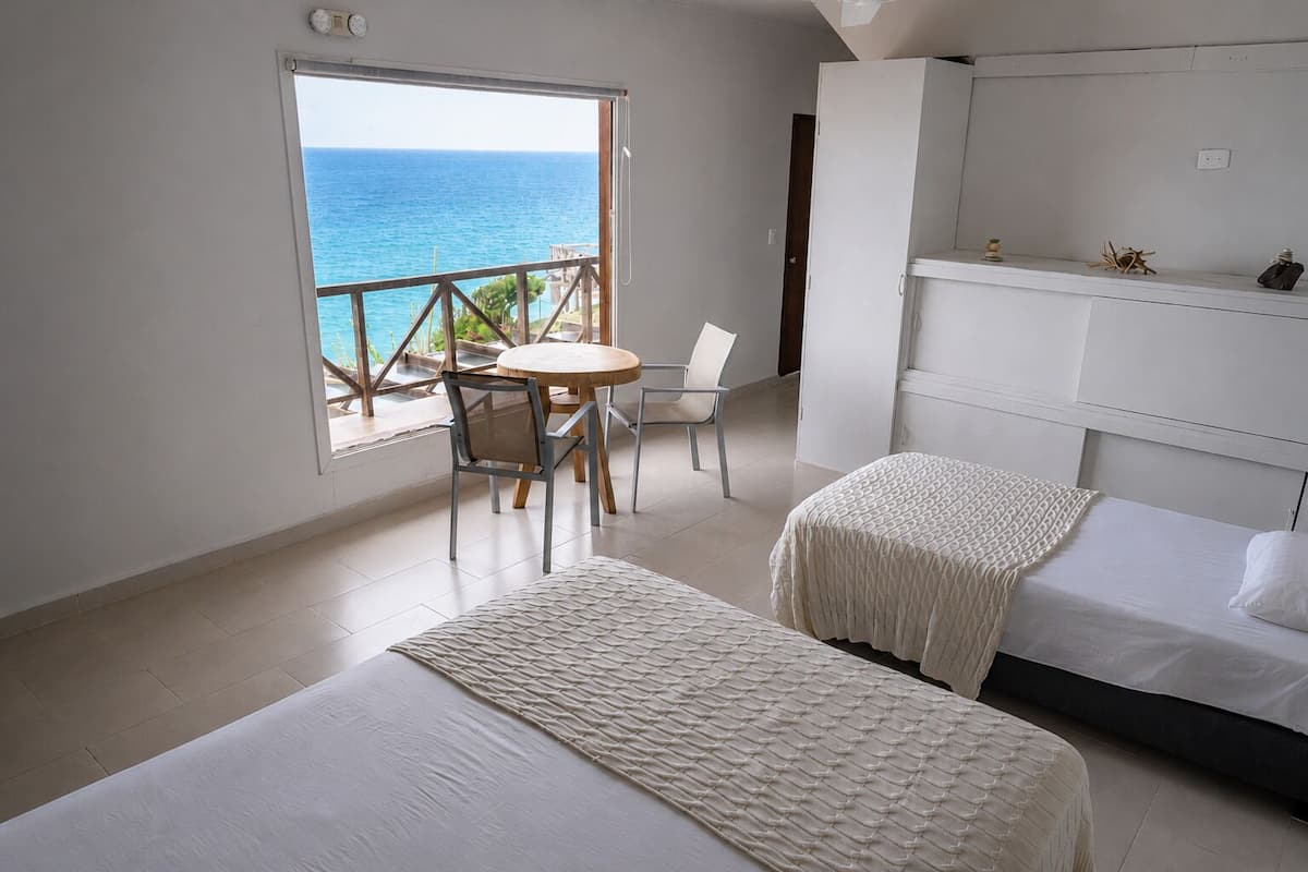 Une chambre avec deux lits, une petite table et une chaise, donnant sur la mer grâce à un balcon.