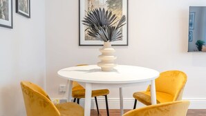 Ein Essbereich mit einem runden weißen Tisch, gelben Stühlen und einer Pflanze in einer Vase.