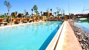 A swimming pool with lounge chairs and umbrellas, surrounded by palm trees and buildings. - Splendid Apartment in the Jardins de l'Atlas 4620 (Marrakech)