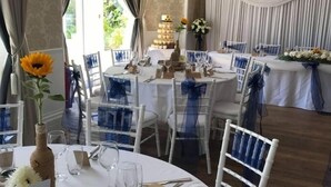 A formal dining room with round tables, white chairs, and blue sashes. - Nethway Hotel (Torquay)