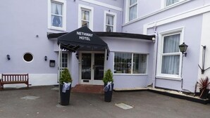 A Nethway Hotel entrance with a black awning, two potted plants, and a bench. - Nethway Hotel (Torquay)