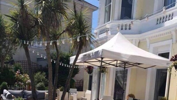 An outdoor seating area with wicker furniture, a white canopy, and palm trees. - Nethway Hotel (Torquay)