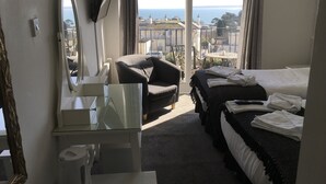 A hotel room with a bed, a chair, a desk with a mirror, and a view of the sea. - Nethway Hotel (Torquay)