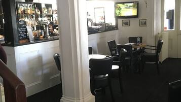 A bar area with a counter displaying various bottles, a television mounted on the wall, and a seating area with tables and chairs.