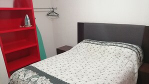 Quarto com uma cama, uma estante vermelha e uma pequena mesa de cabeceira.