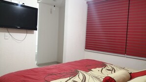 Quarto com cama, televisão na parede e janela com persianas vermelhas.