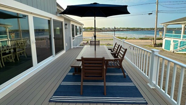 A wooden deck with a table and chairs, a large umbrella, and a view of the beach and ocean. - The Pioneer - York Beachfront living (York)