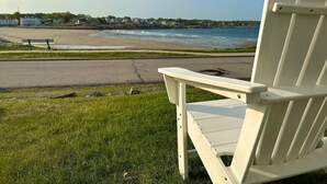 A white Adirondack chair facing a beach with a road and buildings in the background. - The Pioneer - York Beachfront living (York)