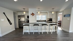 A modern kitchen with a central island, bar stools, and a decorative fish wall art piece. - The Pioneer - York Beachfront living (York)