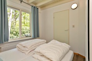 A room with two beds, a window with curtains, a door, and a light fixture.