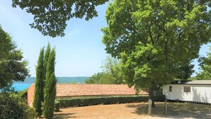 A caravan park with a red-tiled roof building, surrounded by trees and a clear view of the sea. - Les Bastides de Chanteraine (Aiguines)