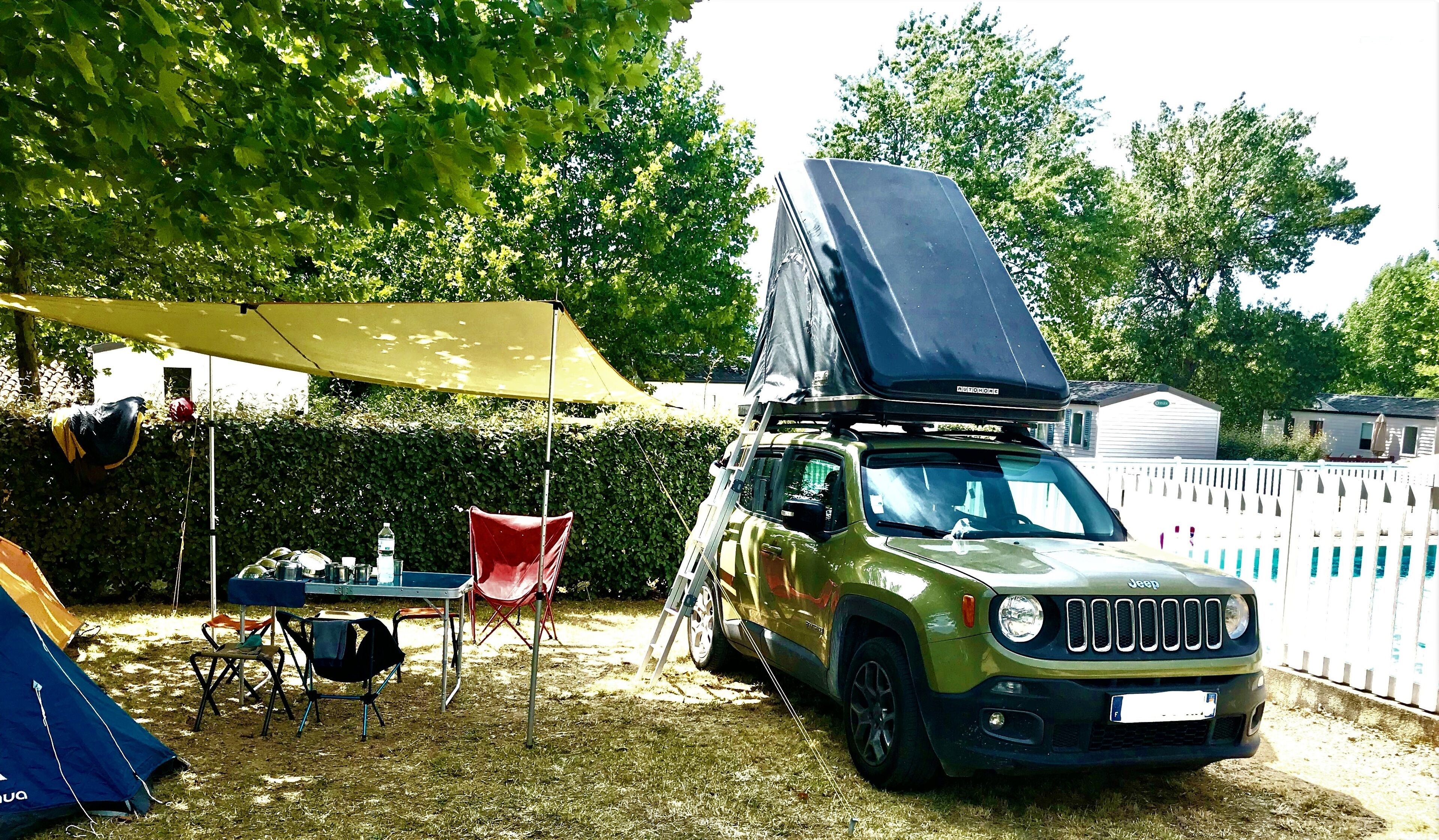 A Jeep parked in a backyard with a tent and camping chairs.
