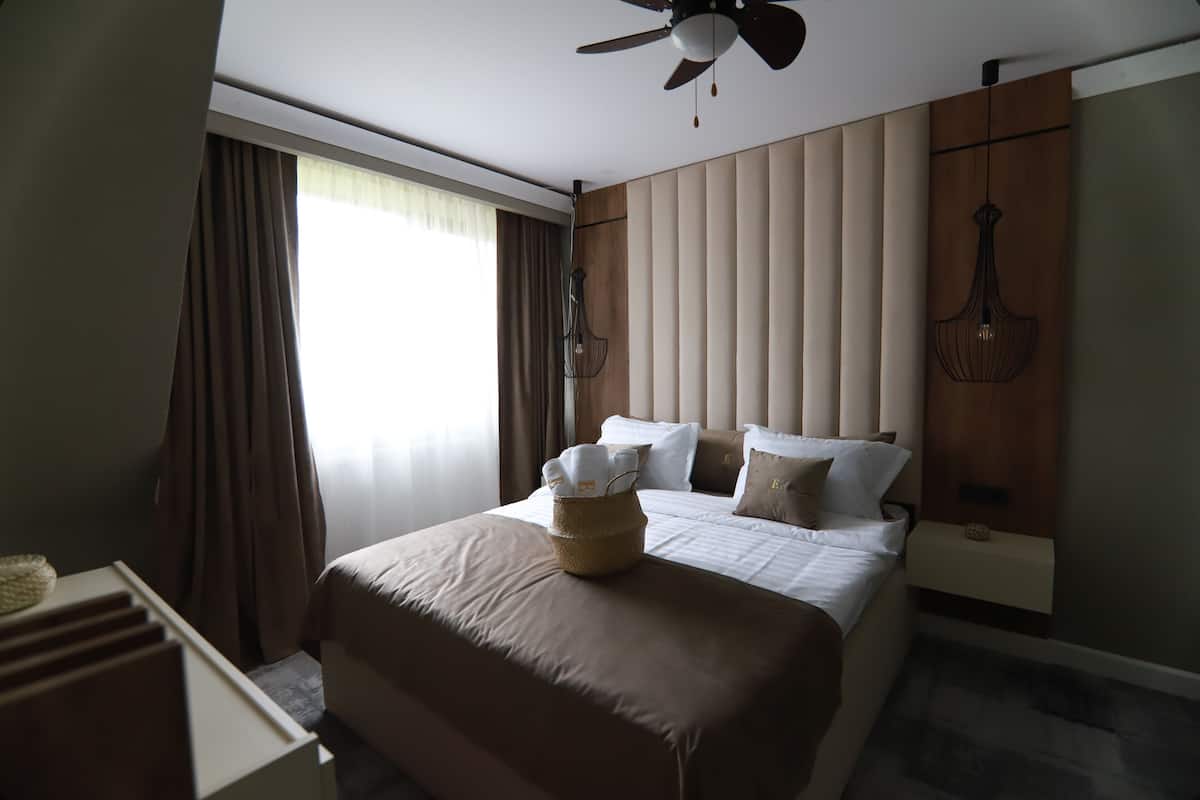 A hotel room with a large bed, a ceiling fan, a bedside table, and a window with curtains.