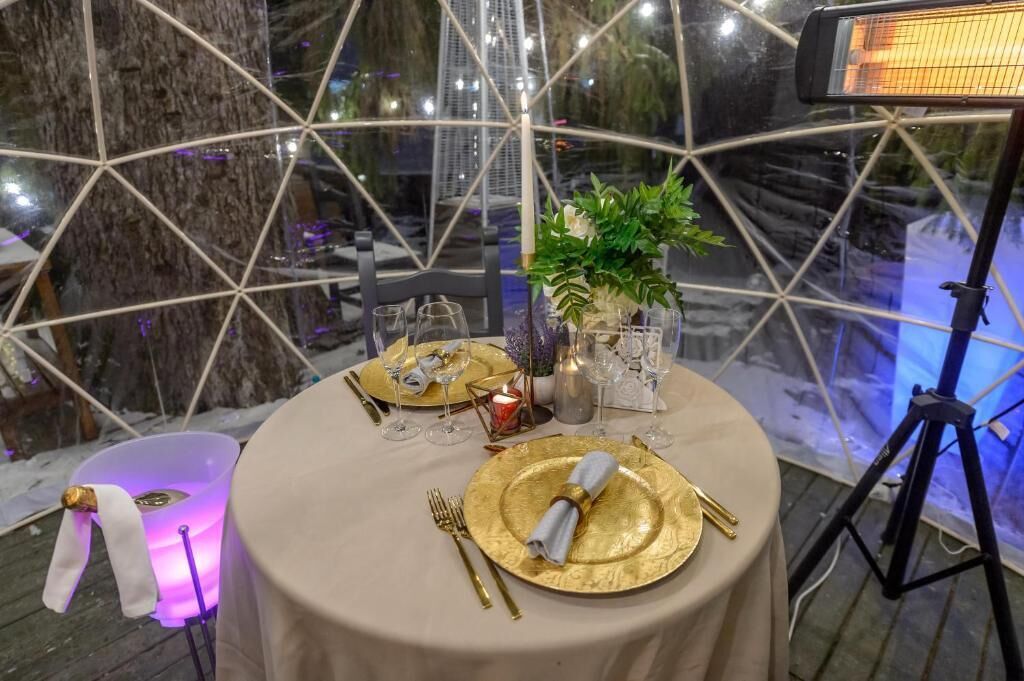Un comedor interior con una mesa redonda dispuesta para dos personas, con platos dorados, cubiertos y un centro de mesa con velas.