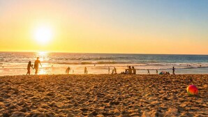 A beach with people walking and playing, and a ball on the sand.