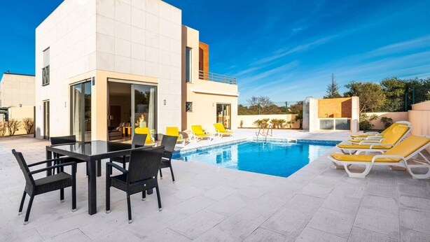 A modern building with a pool area, including a dining table with chairs and lounge chairs around the pool.